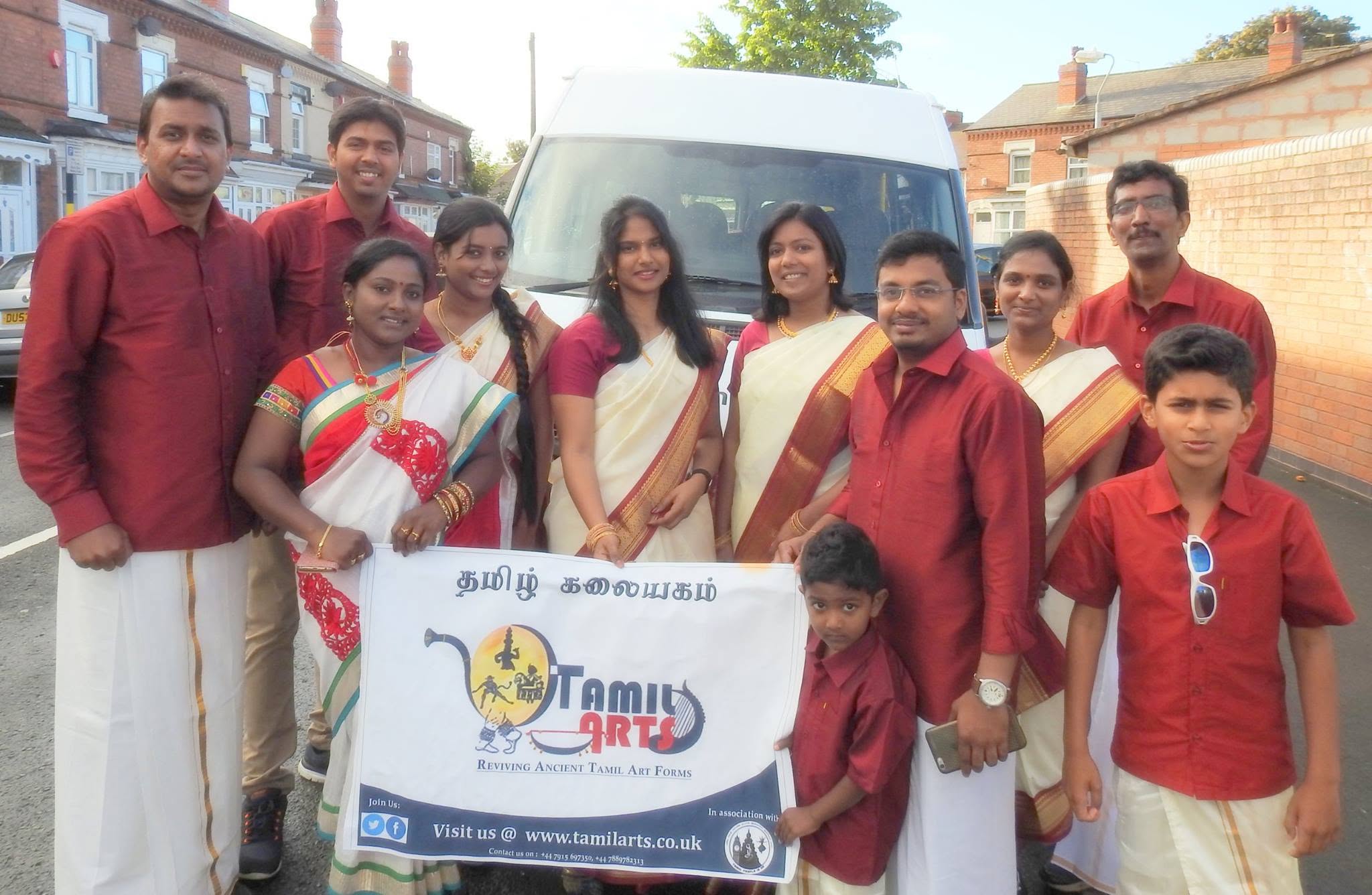 The group in red and white holding the Tamil Arts banner beside a minibus