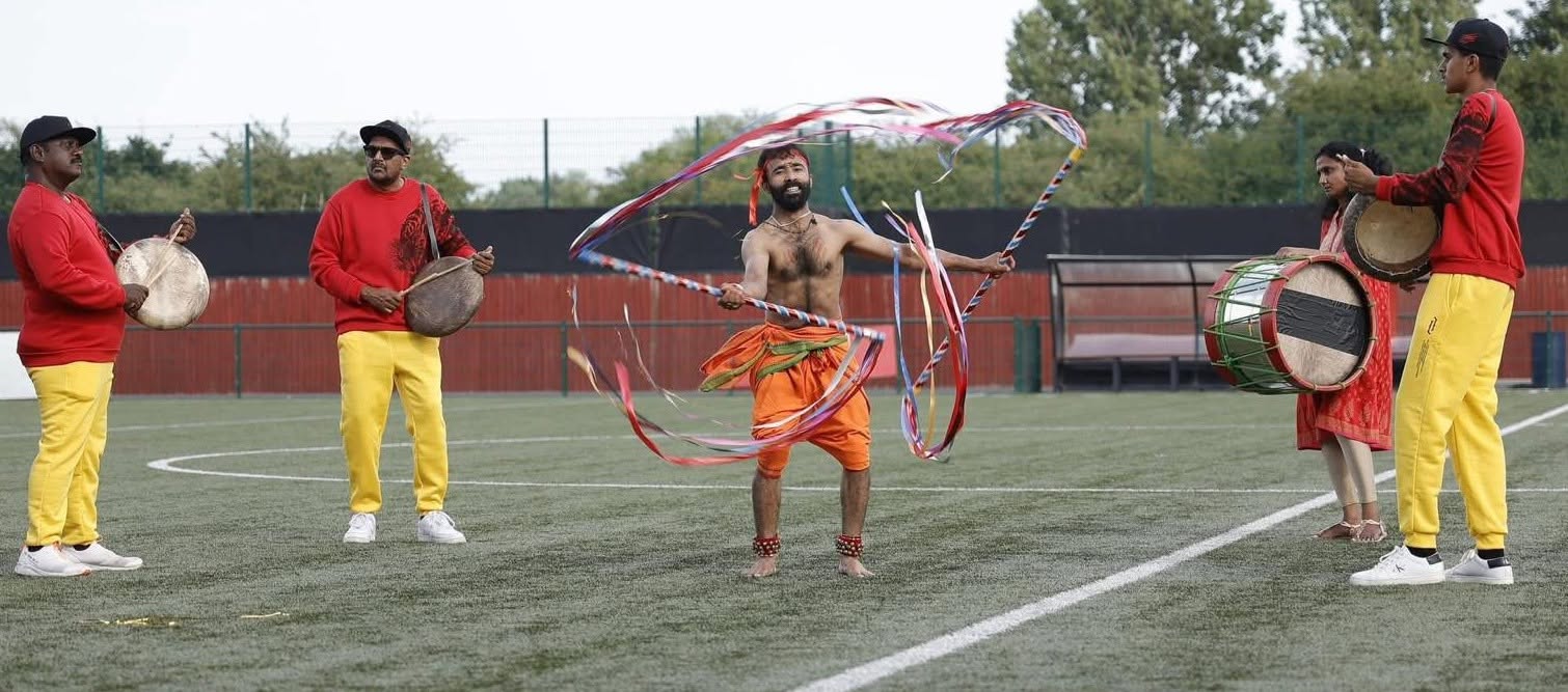 A performer spinning coloured ribbons on an outdoor pitch while a drummer plays