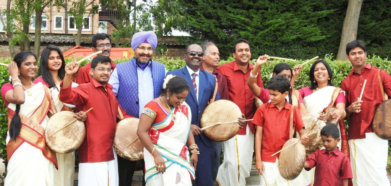 The parai troupe outdoors with invited guests, drums raised and sticks in the air