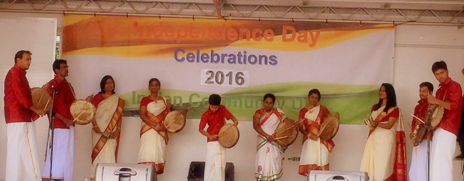 Performers with frame drums in front of an Independence Day Celebrations 2016 banner