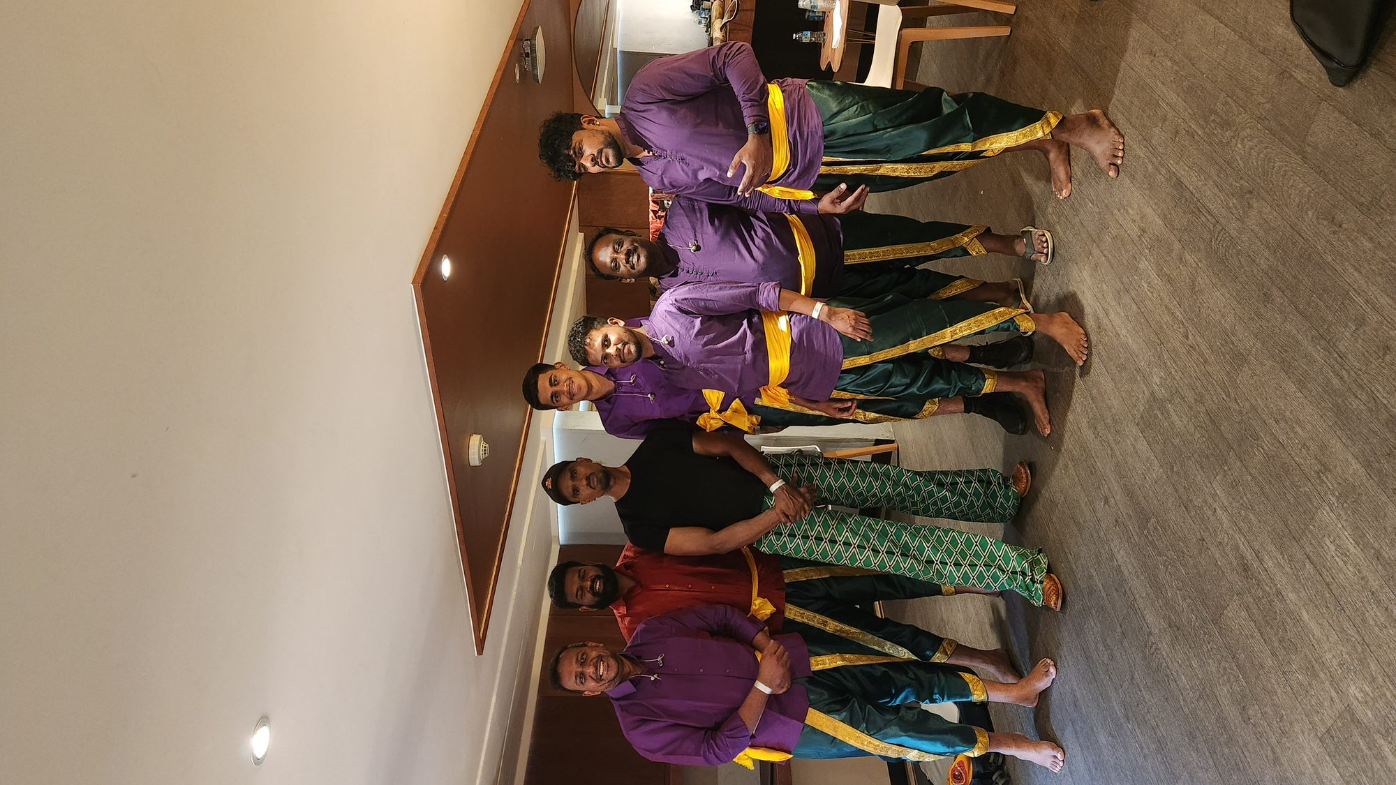 Performers in purple and gold holding silambam sticks indoors