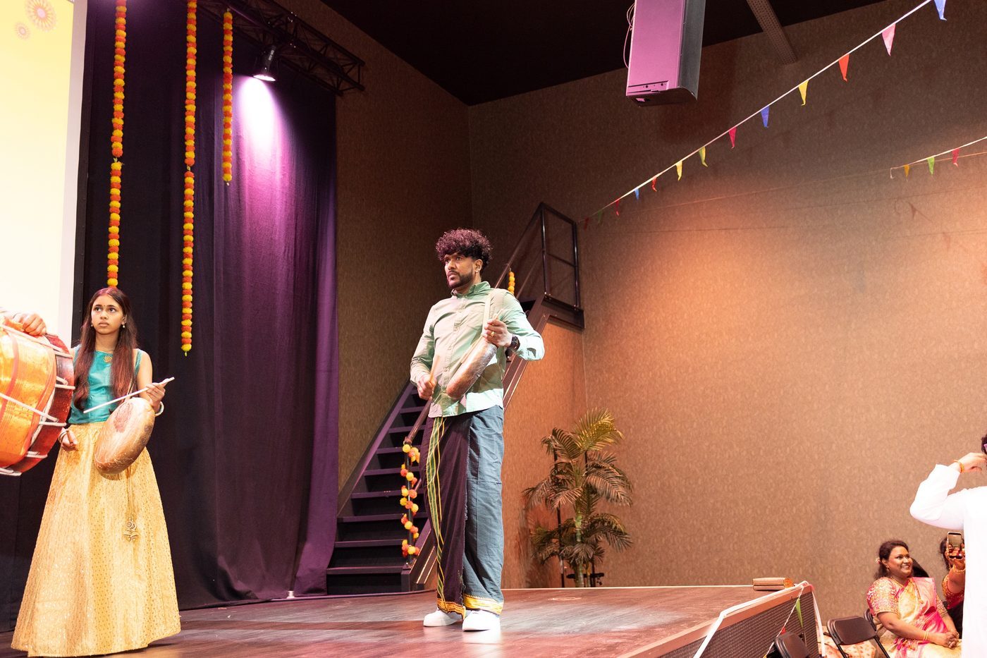 A drummer performing on stage in the Netherlands under marigold garlands and bunting