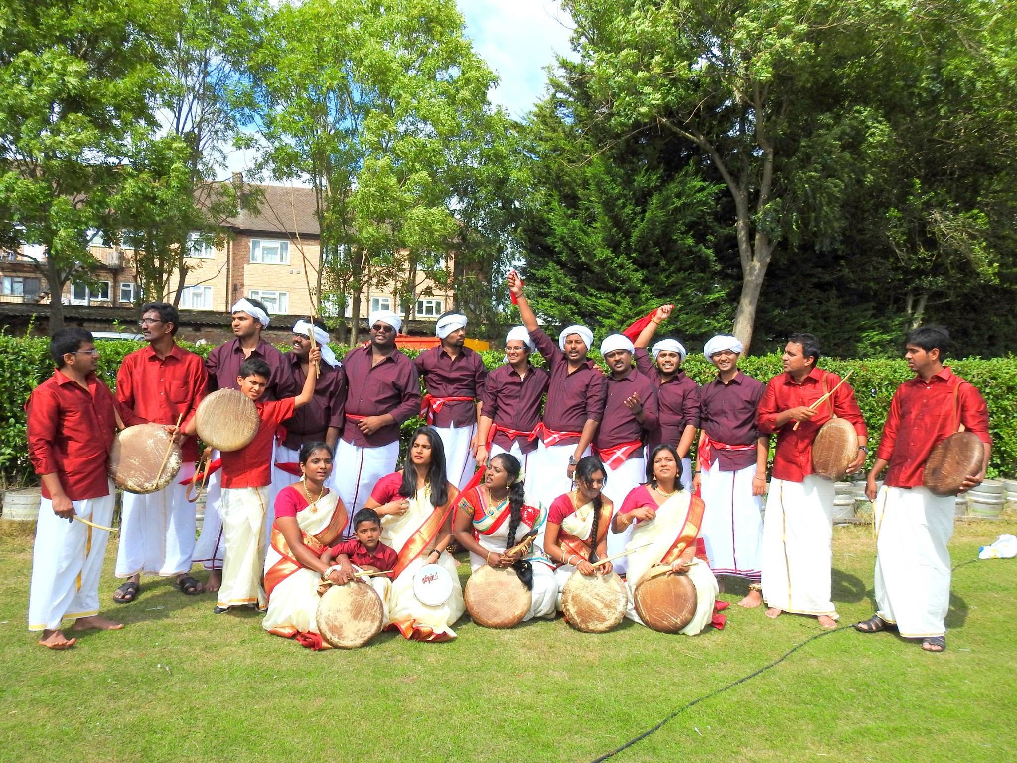 The troupe in maroon and white seated with their drums on a lawn