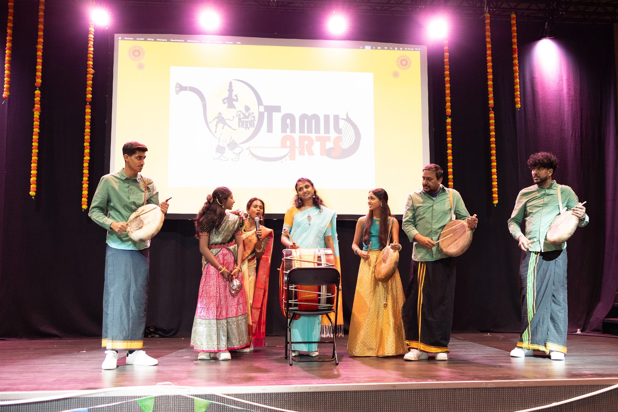The full troupe lined up across the stage with parai drums under the Tamil Arts backdrop