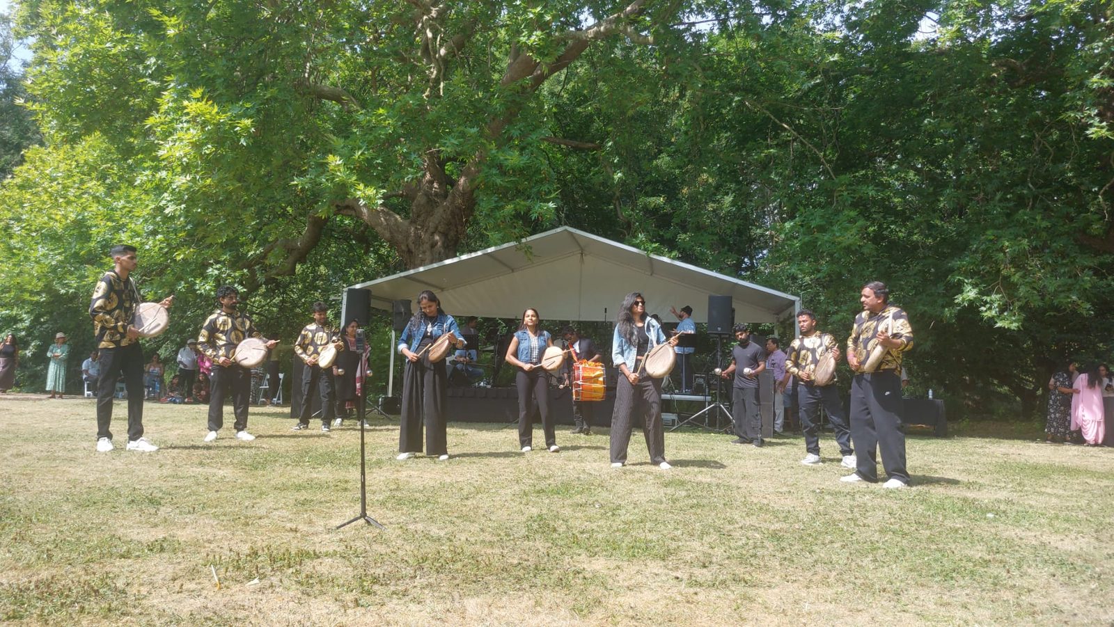 Parai players performing on the grass in front of an open-sided marquee stage at an outdoor summer event